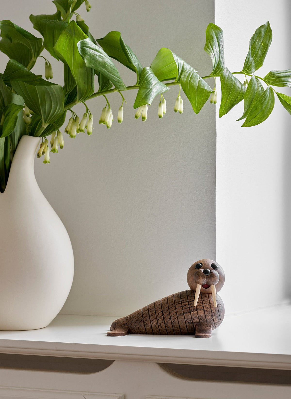 Wally seul posé sur une étagère à côté d’un vase et d’une plante.