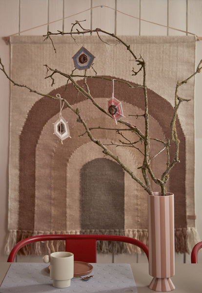 Vase Toppu haut caramel et rose avec des branches devant un tapis mural